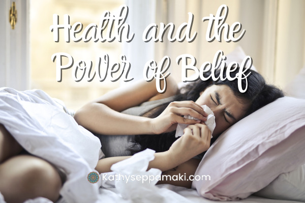 Health and the Power of Belief Blog post title with a picture of a woman laying in bed and blowing her nose