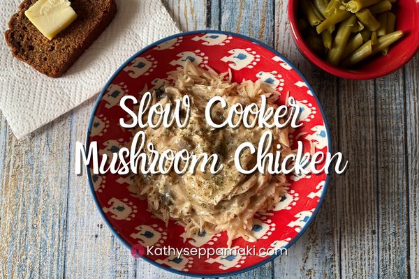 Slow cooker mushroom chicken title with picture of a red bowl containing mushroom chicken. There is bread with butter and green beans in containers off to the side of the bowl.