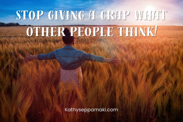 Stop giving a crap what other people think blog post title with a picture of a woman standing in a wheat field in a victorious pose.