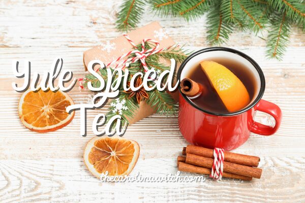 Yule Spiced Tea blog post title with a picture of a cup of tea with cinnamon sticks and orange peel sitting on a table top. Next to it is a festive holiday package and some evergreen boughs.