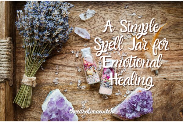 A Simple Spell Jar for Emotional Healing blog post title with a picture of two small spell jars laying on a table surrounded by a branch of lavender, a feather and two pieces of amethyst geode.