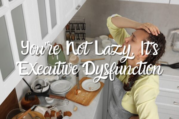 You're Not Lazy, It's Executive Dysfunction blog post title with a picture of a distressed woman standing in front of her kitchen sink looking at the pile of dirty dishes that need to be cleaned.