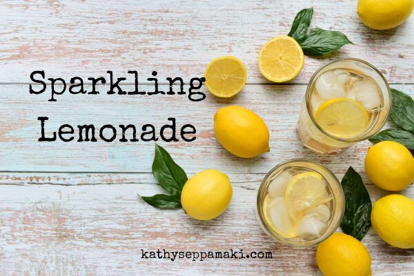Sparkling Lemonade blog post title with picture of two glasses of sparkling lemonade sitting on a table covered with lemons