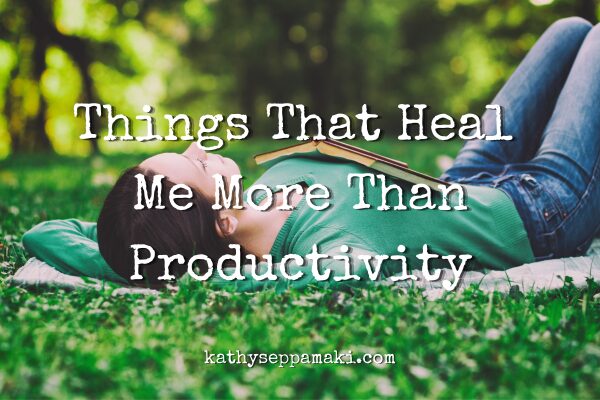 Things That Heal Me More Than Productivity blog post title with picture of a woman laying on her back on a blanket on the grass covered ground. She has an open book laying on her chest and her eyes are closed.